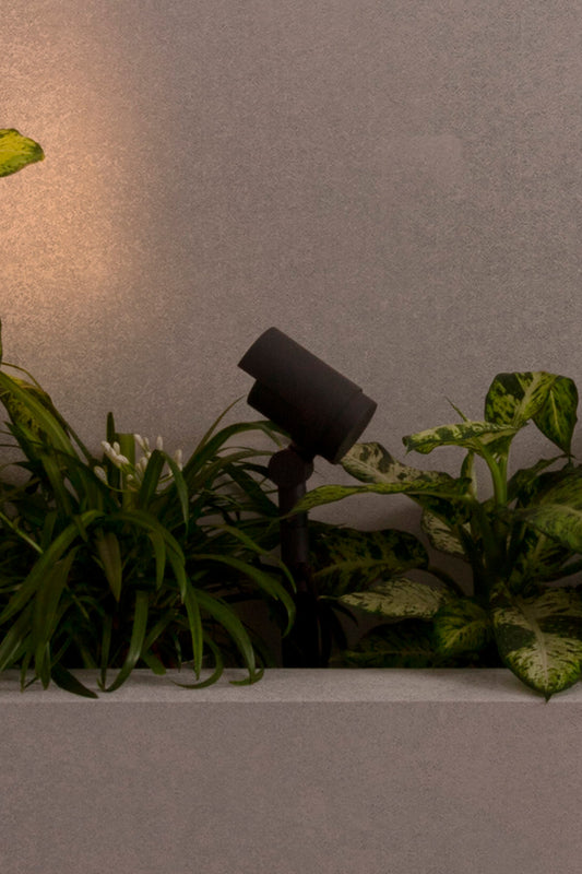 Lámpara proyector estaca FOC 210 gris oscuro FARO 70158 en ambiente de jardín exterior, luminaria LED IP65 orientable iluminando terraza y superficie.