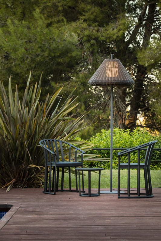 Lámpara de pie exterior SAIGON OUT 1950 W70 de FARO en gris y marrón, con estructura de aluminio y mimbre sintético, iluminando un jardín o terraza en ambiente nocturno