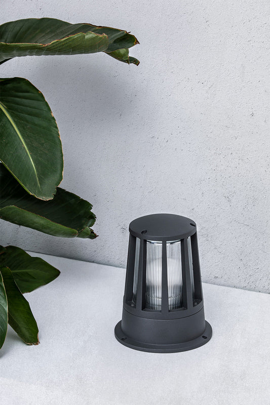 Baliza exterior SURAT gris oscuro modelo FARO 72310 en ambiente de jardín y terraza, luminaria de superficie en aluminio y cristal con protección IP54 para iluminación exterior