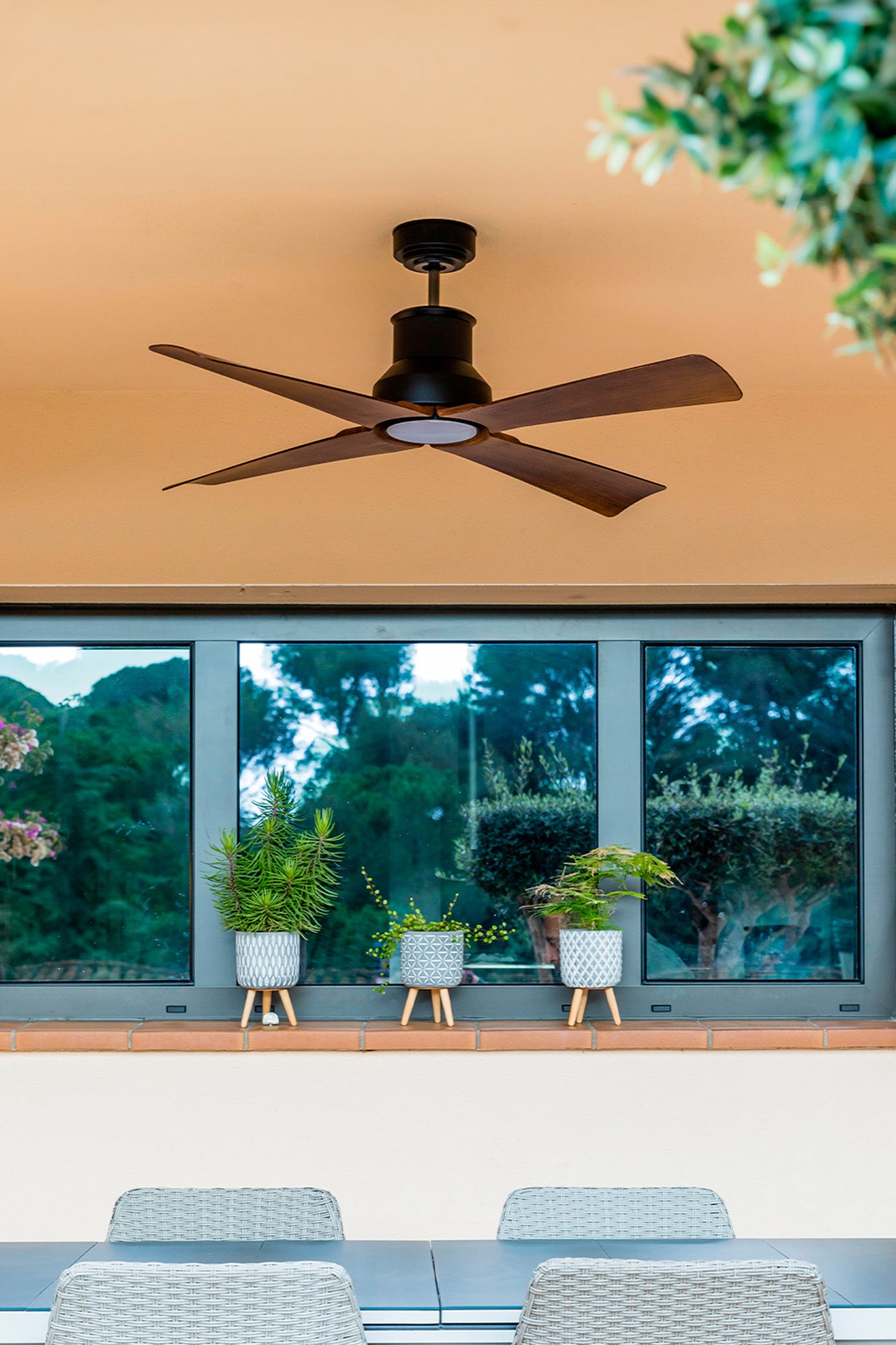 Ventilador de techo WINCHE M en negro y marrón de FARO modelo 33481 con protección IP44 para exteriores, motor DC eficiente, mando a distancia y función inversa, en ambiente acogedor de patio cubierto con ventilación natural.