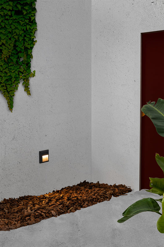 Lámpara de pared LED GRANT SQ Aplique en gris oscuro, modelo FARO 70655, instalada en terraza exterior iluminando jardín por la noche, diseño en ABS y policarbonato para señalización LED.