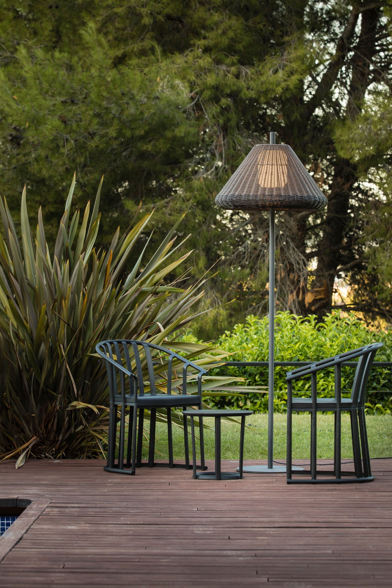 Lámpara de pie exterior SAIGON OUT 1950 W70 de FARO en gris y marrón, con estructura de aluminio y mimbre sintético, iluminando un jardín o terraza en ambiente nocturno