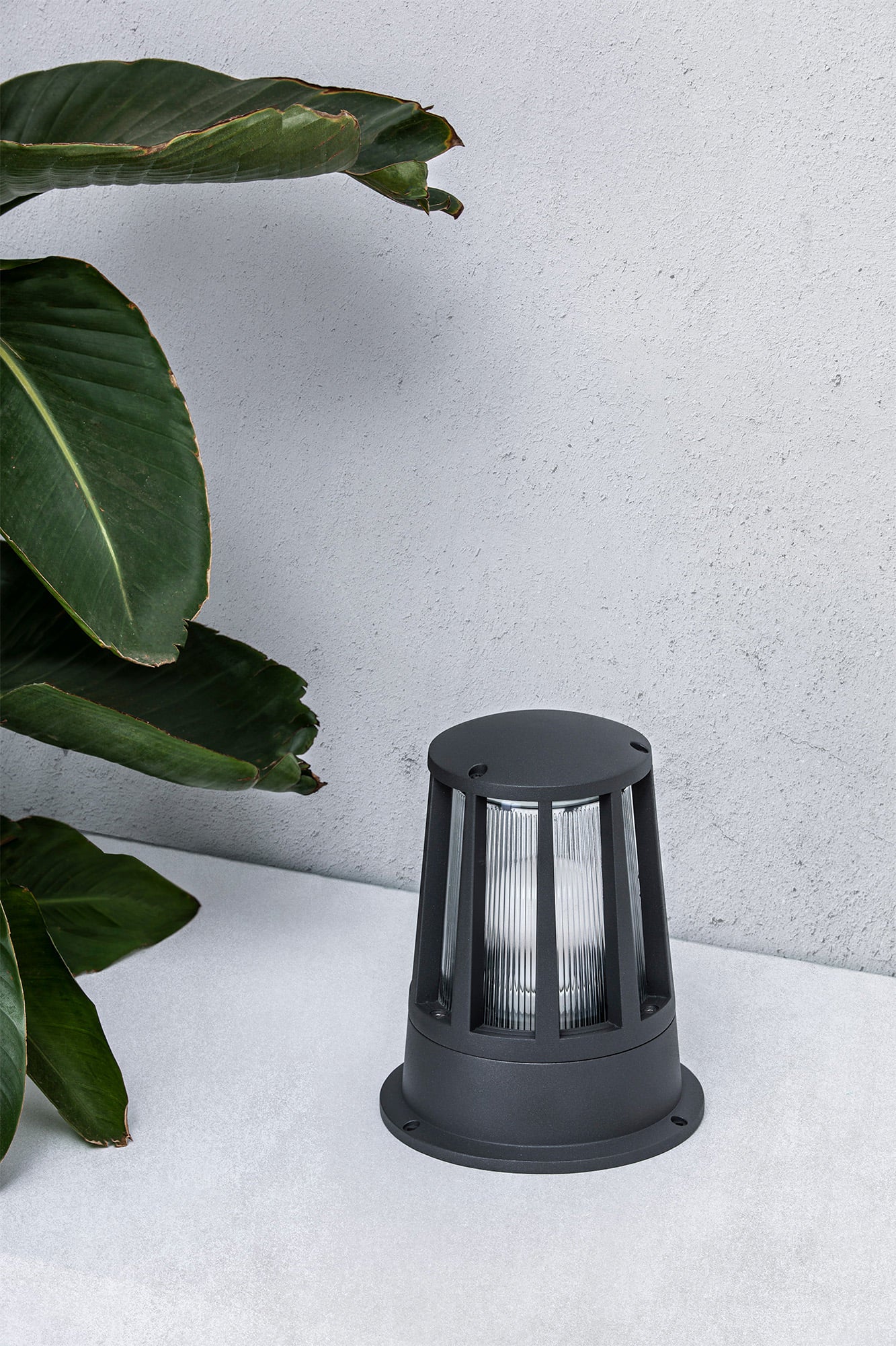 Baliza exterior SURAT gris oscuro modelo FARO 72310 en ambiente de jardín y terraza, luminaria de superficie en aluminio y cristal con protección IP54 para iluminación exterior