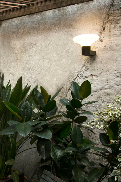 Aplique de pared exterior BLUBS Gris Oscuro FARO 74432A-03 en ambiente de jardín iluminado, luminaria contemporánea de aluminio y PMMA IP44 para exteriores
