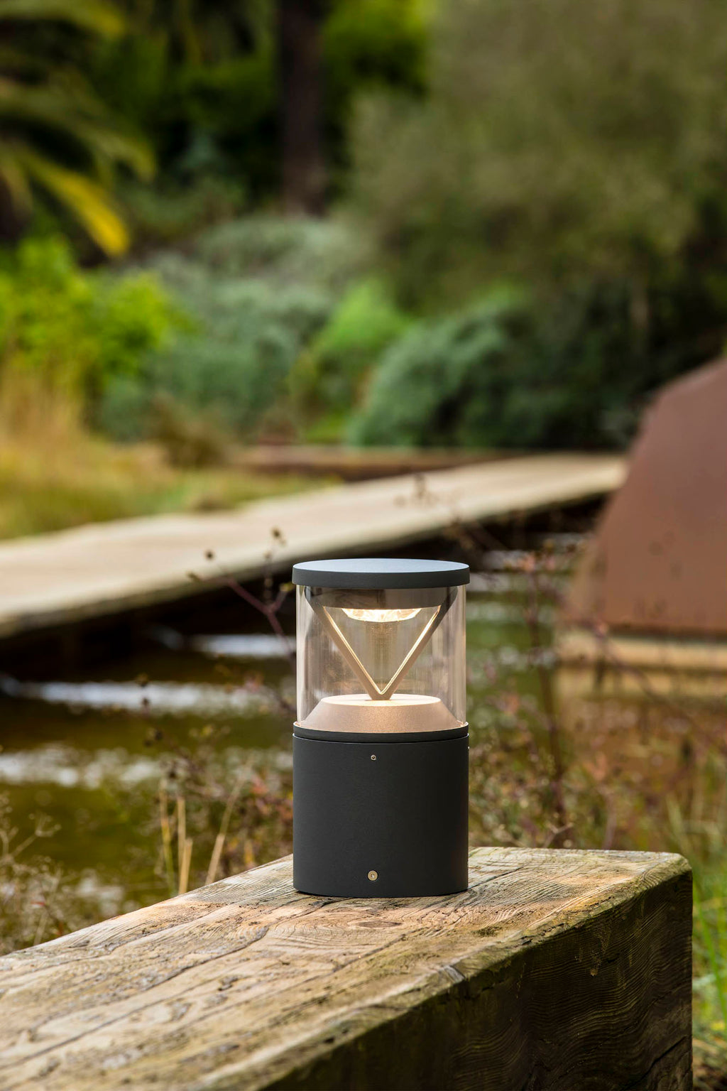 Luminaria sobremuro exterior RUSH 250 gris oscuro 3000K de FARO modelo 750012C, instalada en jardín o parque con aluminio y PC, compatible CASAMBI para iluminación ambiental.