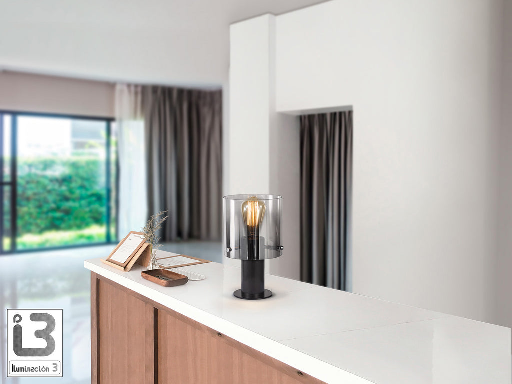 Lámpara de sobremesa Venize negro smoke de Schuller, ideal para dormitorio o salón. Diseño moderno e industrial con cristal smoke y metal negro satinado. Utiliza bombilla E27 (12837).